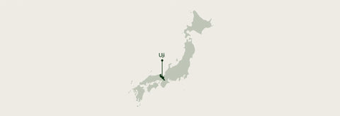 A minimalist map graphic of Japan on a light warm gray background, with a small dark green pin marking a location and the text 'Uji' above it.